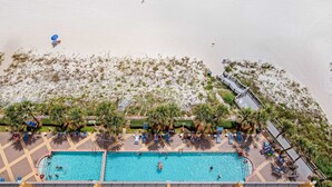 Luchtbeeld van een resort met zwembad, strand en palmbomen.