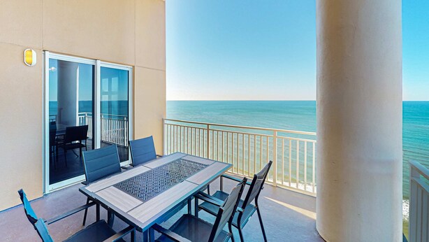 Ein Balkon mit Tisch und Stühlen, eine Glastür, die zu einem Innenbereich führt, und Blick aufs Meer.