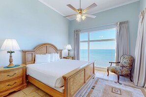 Ein Schlafzimmer mit Bett, Nachttischen, einem Sessel und einem Deckenventilator, mit Blick auf den Ozean.