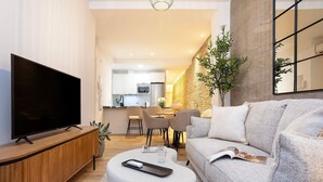Una sala de estar moderna con una televisión de pantalla plana, un sofá, una mesa de centro y un área de comedor al fondo.