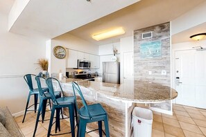 A modern kitchen with a central island, bar stools, and a clock on the wall. - Beachfront condo with amazing Gulf views, balcony, pools, hot tubs, gym, & sauna (Panama City Beach)