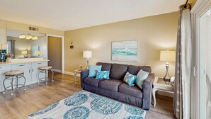 Un salon avec un canapé marron foncé, un tapis à motifs et un tableau accroché au mur.