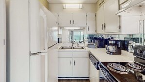 Une cuisine de taille réduite avec des meubles blancs, une cuisinière encastrée et une machine à café.