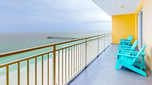 A balcony with a view of the ocean, a pier, and turquoise chairs. - Beachfront condo with stunning Gulf views, beach access, pool, balcony & AC (Panama City Beach)