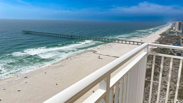 A beach with a pier extending into the ocean, a sandy shore, and a building adjacent to the beach. - Beachfront condo with stunning Gulf views, beach access, pool, balcony & AC (Panama City Beach)