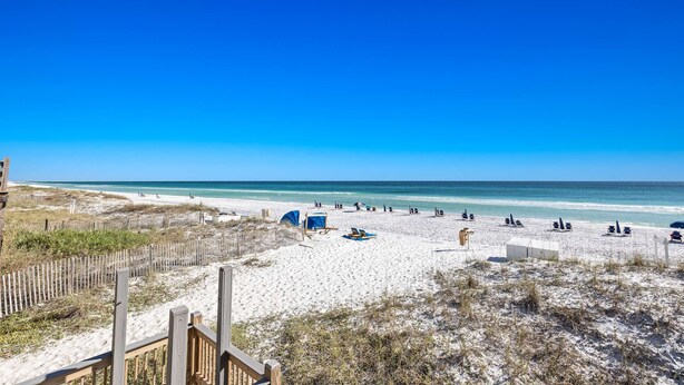 Een strand met een houten hek, ligstoelen en parasols.