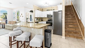 Een moderne keuken met een centraal eiland, roestvrijstalen apparatuur en een houten trap.