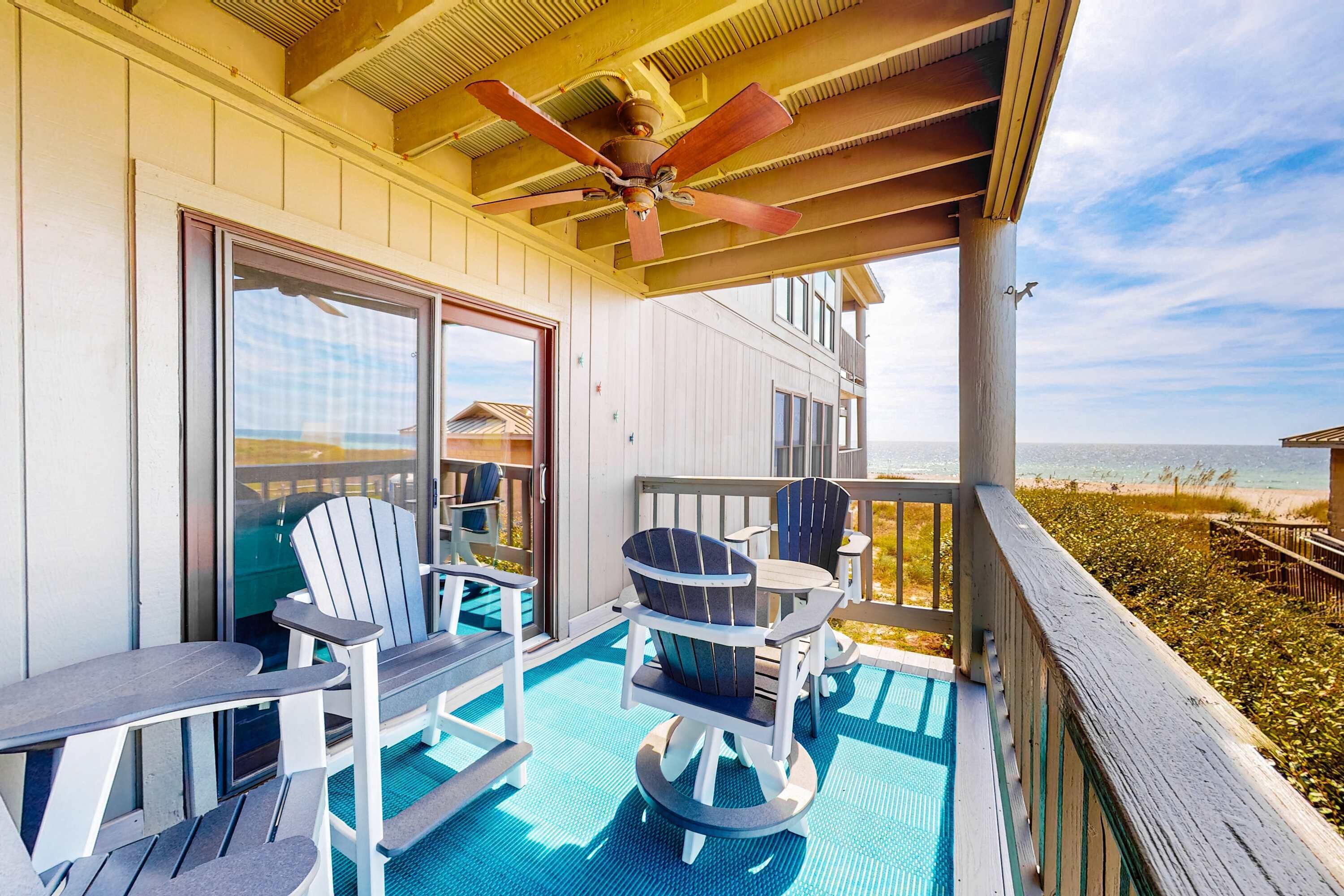 A covered outdoor deck with Adirondack chairs, a ceiling fan, and a view of the beach.