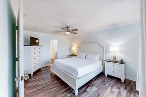 A bedroom with a white bed, a nightstand with a lamp, a ceiling fan, and a sign that reads "BEACH HOUSE." - Ideally located coastal condo with Gulf views, private balcony & beach access (Perdido Key)
