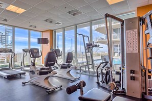 A gym with cardio machines, weight training equipment, and a large window with a city view. - Beachfront 10th-floor condo with Gulf view, pool, gym, & balcony (Perdido Key)