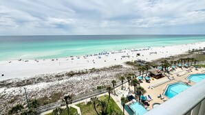 A beach view with a pool area, palm trees, and a clear sky. - Snowbird-friendly condo with panoramic beach & Gulf views - pools, gym (Panama City Beach)