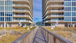 A wooden boardwalk leading to a modern building with multiple balconies and large windows. - Elegant, Gulf-Front Condo w/ Large Balcony, Beach Access & Shared Pool/Gym (Perdido Key)