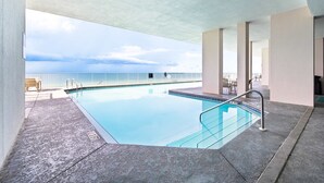 An indoor swimming pool with clear blue water, surrounded by a concrete deck and a covered area with a view of the ocean. - Inviting Gulf-front condo In Perdido Key with waterfront pool/hot tub and oceanfront balcony (Perdido Key)