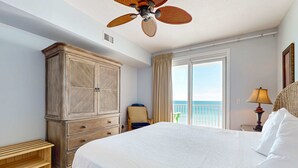 A bedroom with a large bed, a wardrobe, a ceiling fan, a chair, a lamp, and a view of the ocean through a window. - Inviting Gulf-front condo In Perdido Key with waterfront pool/hot tub and oceanfront balcony (Perdido Key)