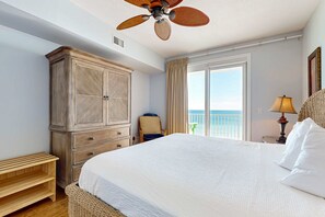Ein Schlafzimmer mit einem großen Bett, einem Kleiderschrank, einem Deckenventilator, einem Sessel, einer Lampe und Meerblick durch ein Fenster.