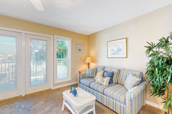 A living room with a striped sofa, a small table with a decorative fish, and a large plant. - Sunny condo with pool, hot tub, pool views, balcony, & AC (Perdido Key)