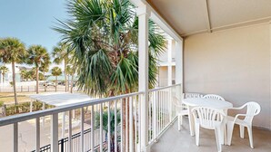 Un balcon avec des chaises blanches et une table, d’où l’on peut admirer des palmiers et une rue.