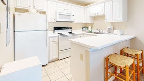 Une cuisine moderne avec des meubles blancs, un four à micro-ondes encastré, une cuisinière et un coin bar avec des tabourets.