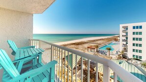 Un balcone con poltrone Adirondack color turchese che si affaccia su una spiaggia e una zona piscina.