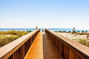 A wooden boardwalk leading to a beach with umbrellas and people in the distance. - 2nd-floor, updated condo with Gulf-front views - short drive to shopping (Fort Walton Beach)