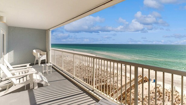 Un balcone con sedie bianche e un tavolino, con vista su una spiaggia e una passerella in legno e una recinzione.