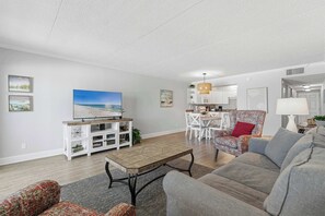 Una sala de estar moderna con un televisor de pantalla plana, un sofá, un sillón estampado y un comedor con una araña.