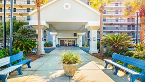 A building entrance with a covered walkway, benches, and palm trees. - Cozy Gulf-front condo with 2 beach chairs - close to entertainment (Fort Walton Beach)