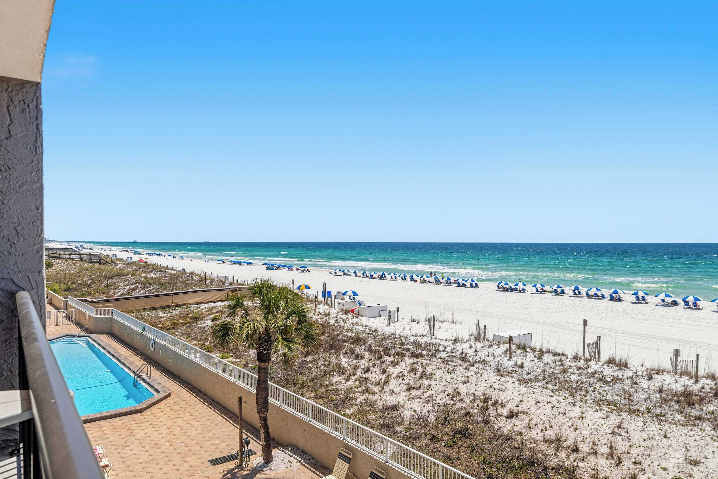 A beach view with a pool, beach umbrellas, and lounge chairs.