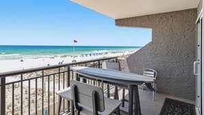 A balcony with a view of the beach, a flag, and outdoor seating. - Cozy Gulf-front condo with 2 beach chairs - close to entertainment (Fort Walton Beach)