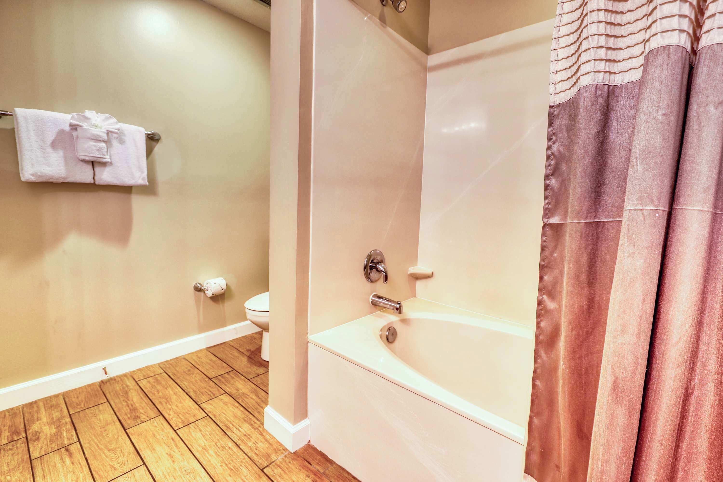 Un baño con piso de madera, una bañera, un inodoro y un perchero con toallas.