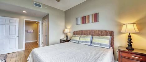 A bedroom with a bed, two bedside tables with lamps, a ceiling fan, a door, and a small bench.