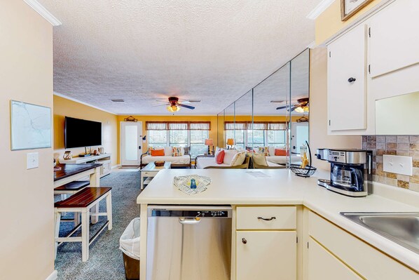 A compact kitchen with a dishwasher, a coffee maker, and a dining area with a bench and table. - Sunny Gulf Coast condo with beach access, pool, tennis, & shuffleboard (Panama City Beach)