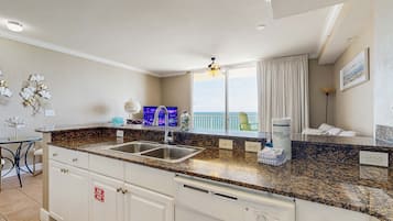 A modern kitchen with granite countertops, a double sink, and a view of the ocean.