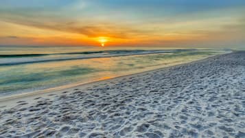 A beach with footprints in the sand and a sunset in the background.
