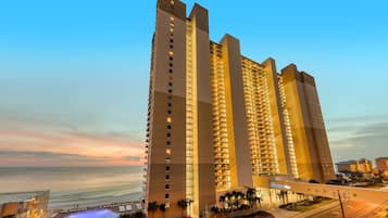 A high-rise hotel with multiple floors, a swimming pool, and a view of the ocean.