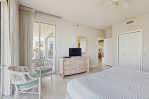 A hotel room with a bed, a television on a dresser, a chair, and a sliding glass door to the outside. - Gorgeous condo with lagoon pool, hot tub, beach access & pickleball court (Seacrest)