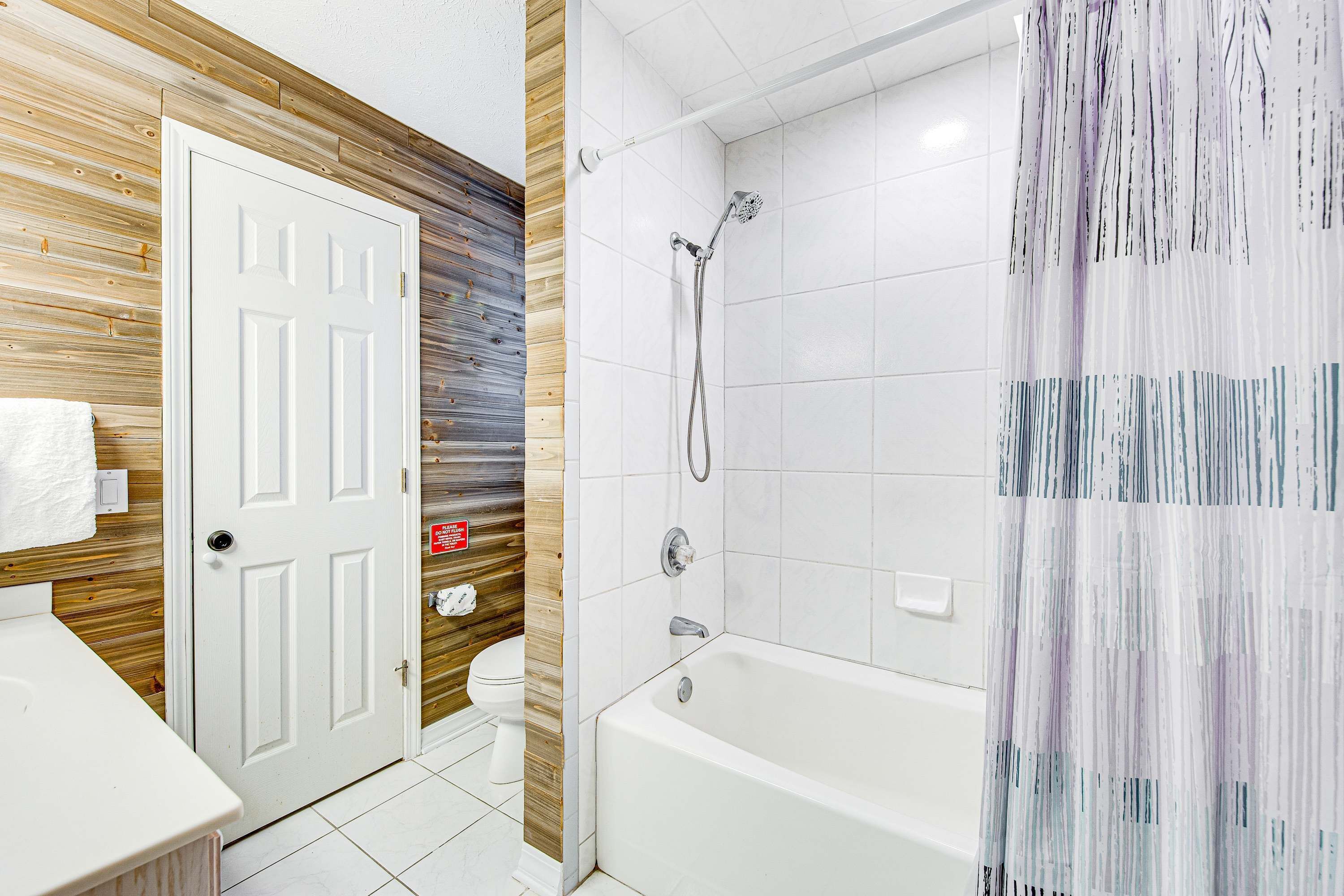 Un baño con pared de madera, puerta blanca, inodoro, bañera y ducha.