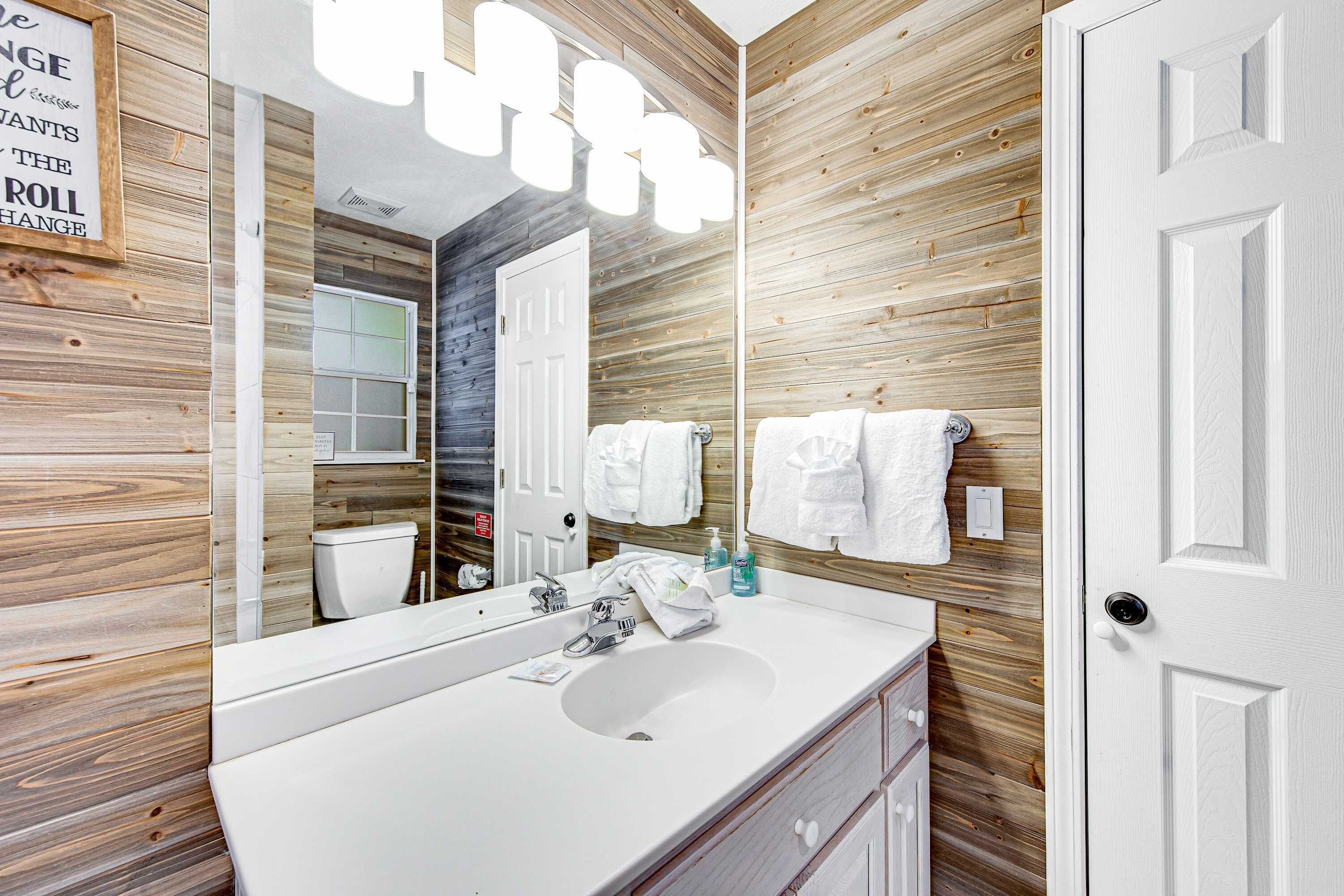 Une salle de bain avec un mur en bois, un lavabo blanc, un miroir et une porte blanche.