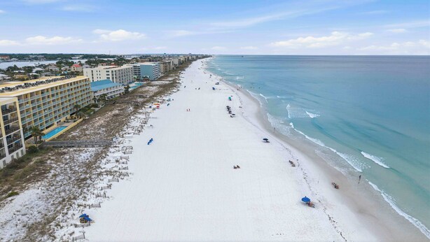 A beach with a hotel on the left, a pier in the distance, and a clear sky. - Oceanfront Condo with Shared Pool & Hot Tub, Ocean View, & Private Washer&Dryer (Fort Walton Beach)