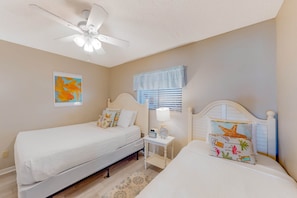A bedroom with two single beds, a ceiling fan, a nightstand with a lamp, and a window with blinds. - Luxury, oceanfront condo with outdoor pool & patio - snowbird-friendly (Miramar Beach)