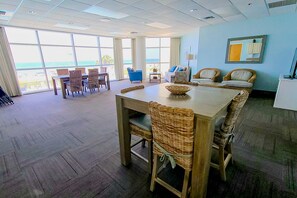 A spacious room with a large dining table and chairs, a sofa, and a view of the ocean through large windows. - Gulf-front condo with amazing views, pools, beach access & gym (Perdido Key)