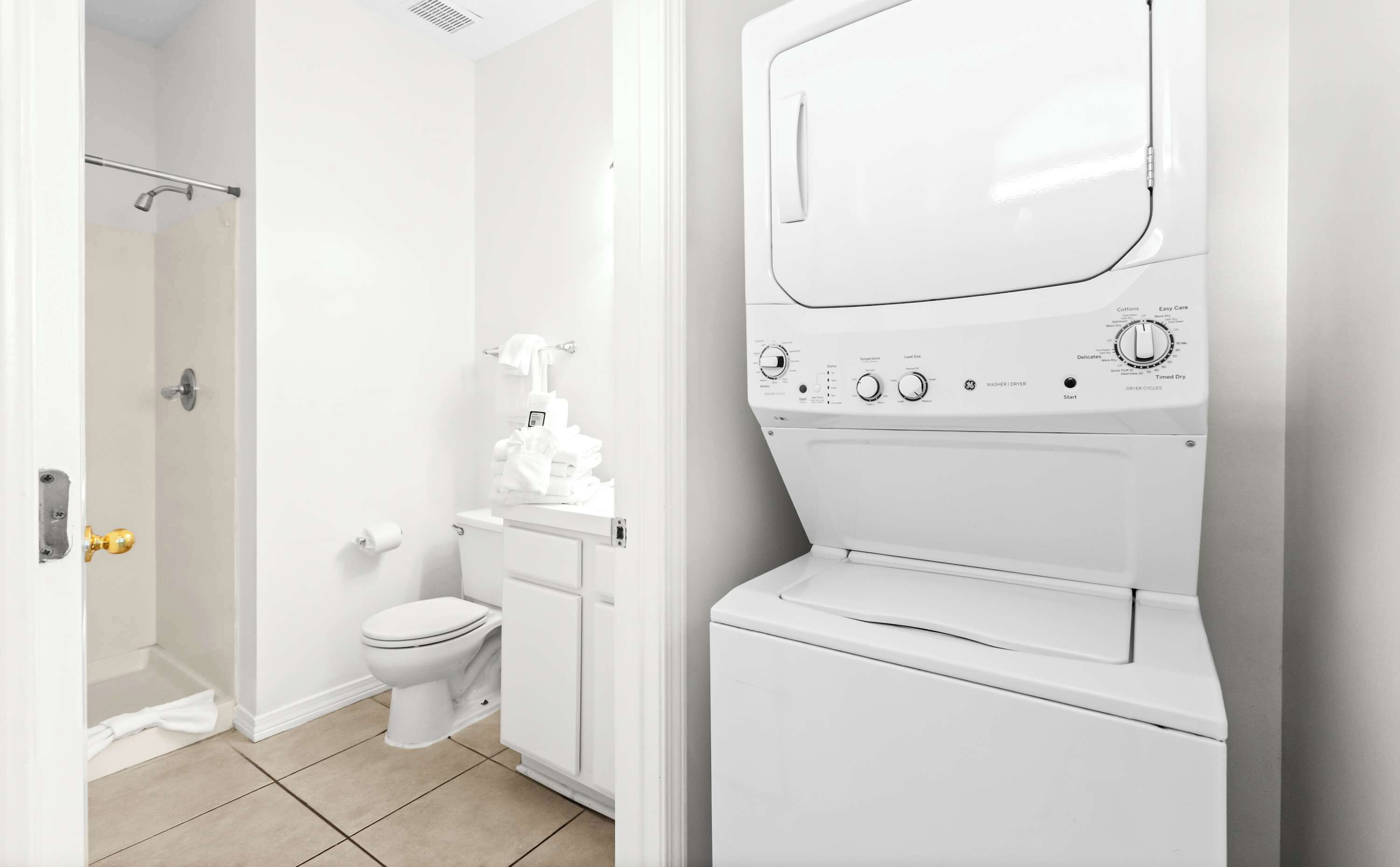 A modern bathroom with a white toilet, a shower area, and a front-loading washing machine.
