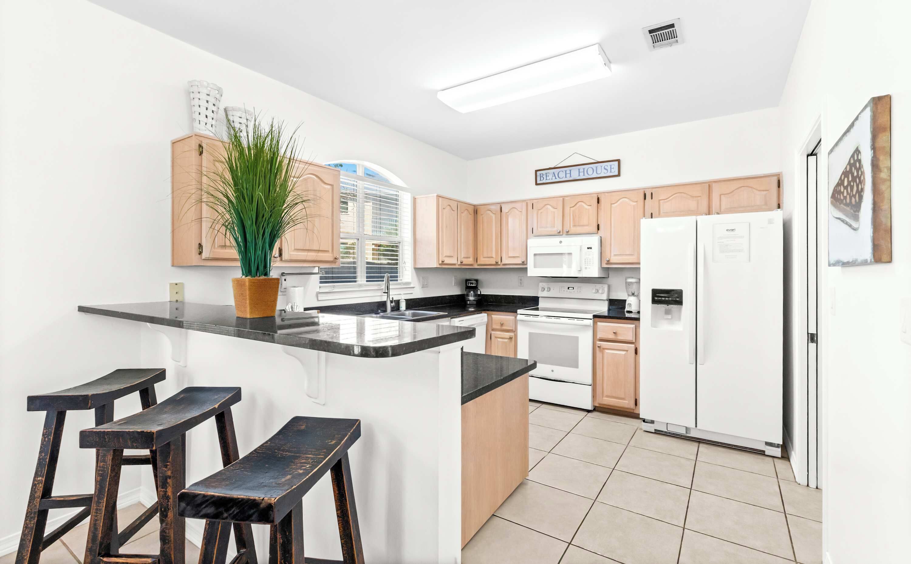 A modern kitchen with wooden cabinets, a black countertop, a white refrigerator, and a potted plant.