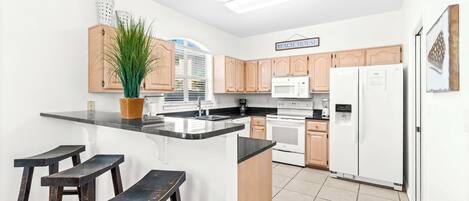 A modern kitchen with wooden cabinets, a black countertop, a white refrigerator, and a potted plant.