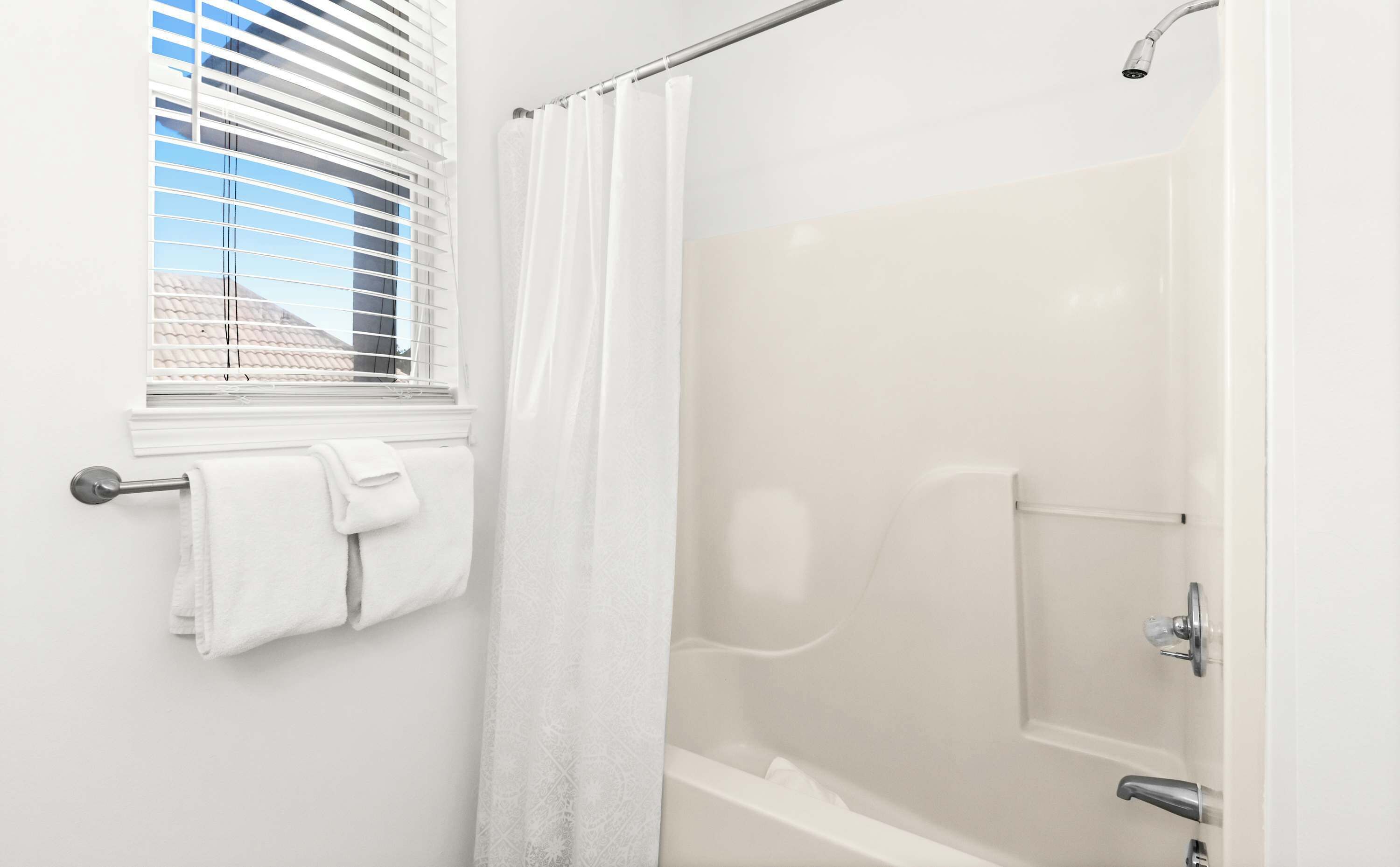 A bathroom with a shower, a window with blinds, and a towel rack with towels.