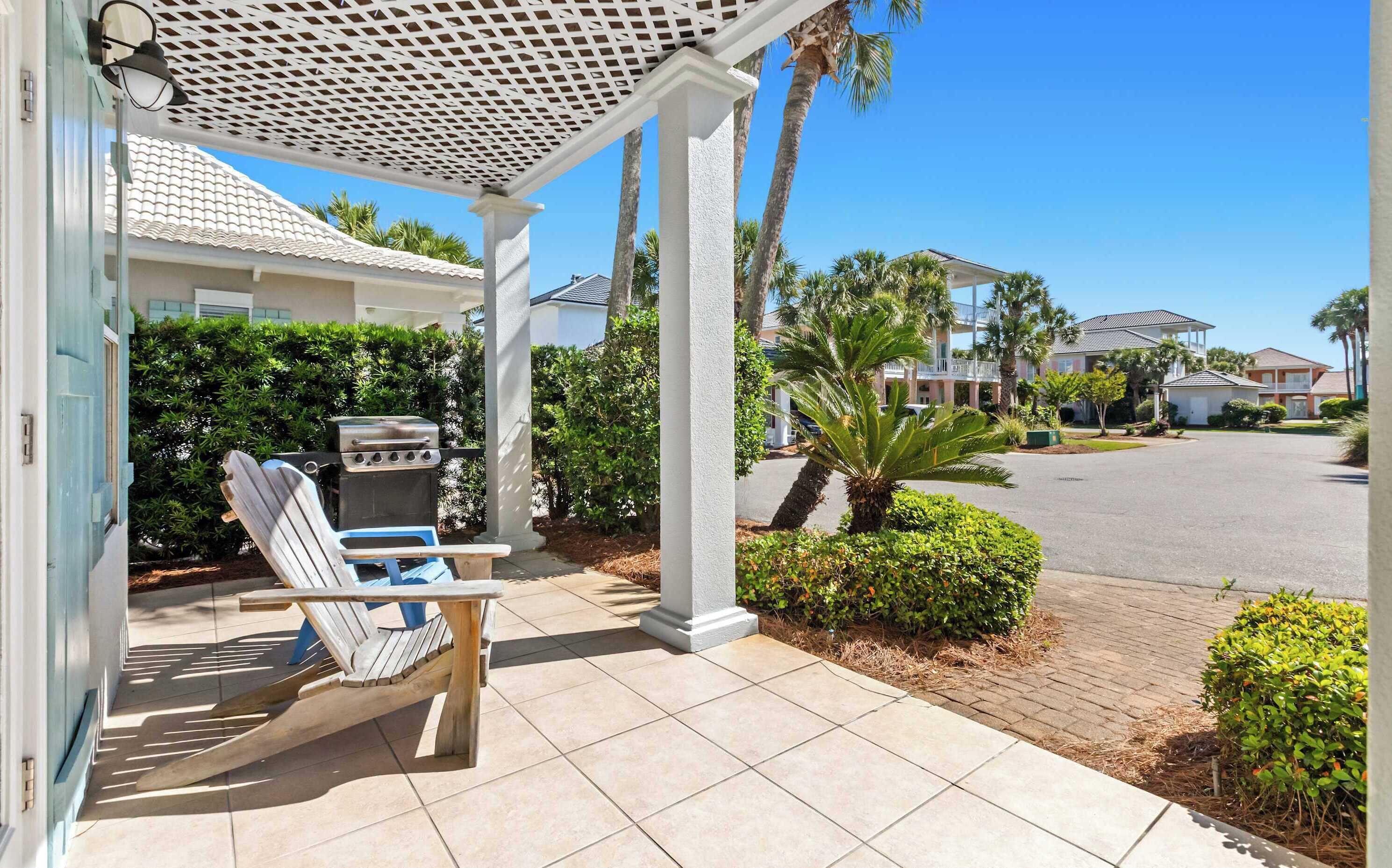 A covered patio with a grill, a wooden chair, and a tiled floor.