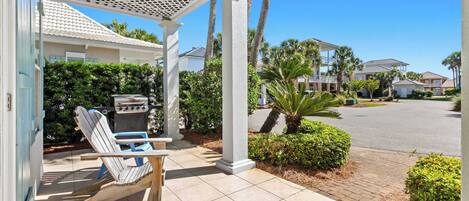 A covered patio with a grill, a wooden chair, and a tiled floor.