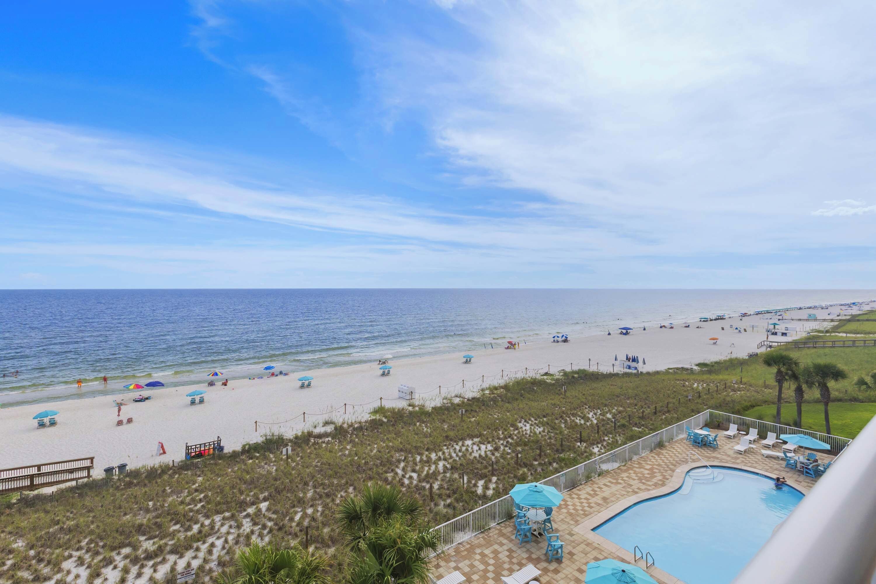 A beach view with a pool area, beach umbrellas, and lounge chairs.