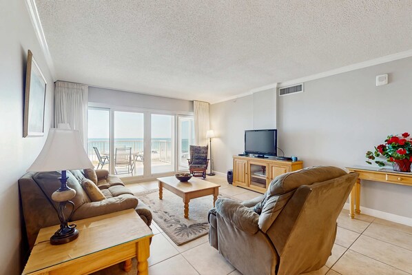A living room with a sofa, a coffee table, a TV, and a balcony with a view. - Gorgeous Oceanfront condo with washer/dryer, Gulf-front balcony & pool/hot tub (Perdido Key)