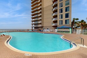 A swimming pool with a 5 ft depth marker, surrounded by a brick deck, and adjacent to a building with balconies. - Remodeled family-friendly, beachfront condo w/ Gulf views, Pool & Hot tub (Panama City Beach)